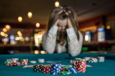 Image of a woman with head in hands at a casino table with gambling chips