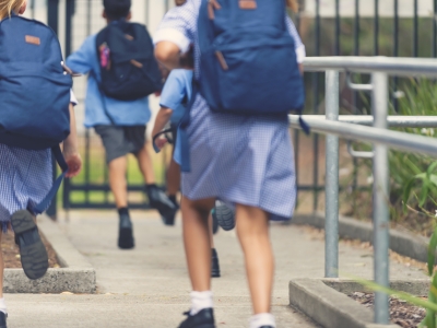 Image of a group of primary school children in uniform running to the school gates.