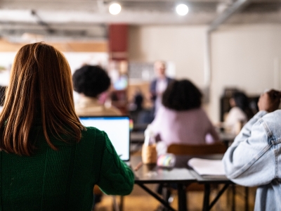 Image of a university class showing a female student with her back to the camera typing on a laptop