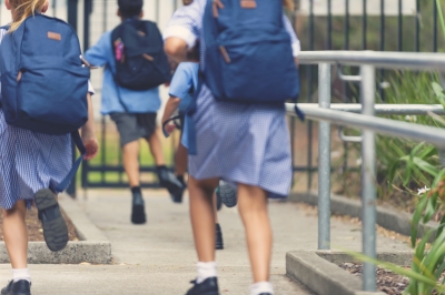 Image of a group of primary school children in uniform running to the school gates.